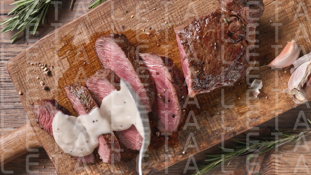 Chef pours pepper sauce on a slices of freshly grilled beef stea