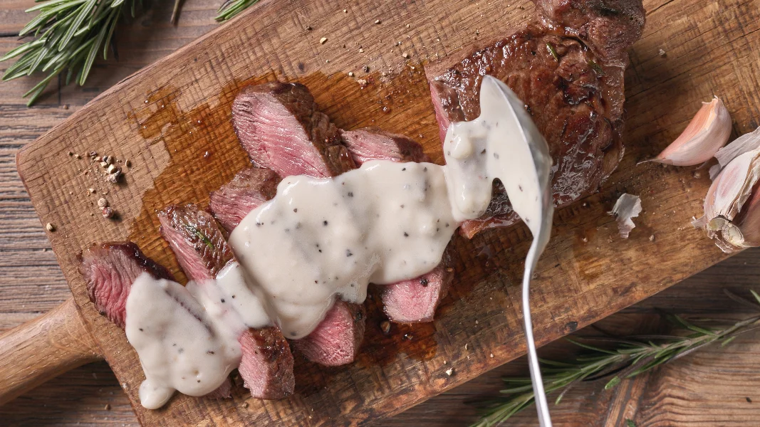 Chef pours pepper sauce on a slices of freshly grilled beef stea