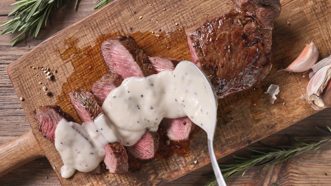 Chef pours pepper sauce on a slices of freshly grilled beef stea