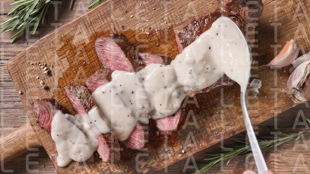 Chef pours pepper sauce on a slices of freshly grilled beef stea