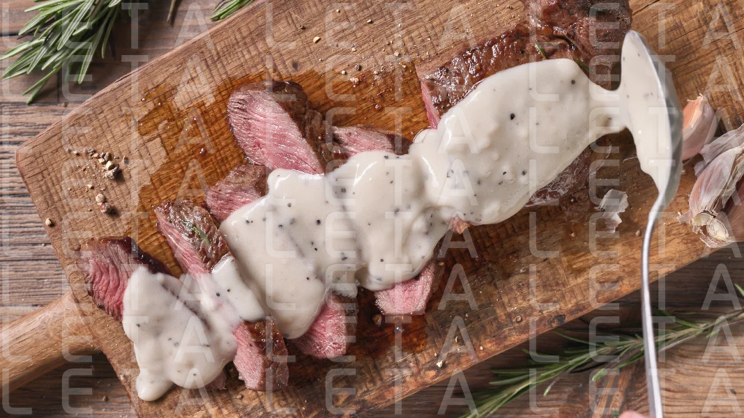 Chef pours pepper sauce on a slices of freshly grilled beef stea