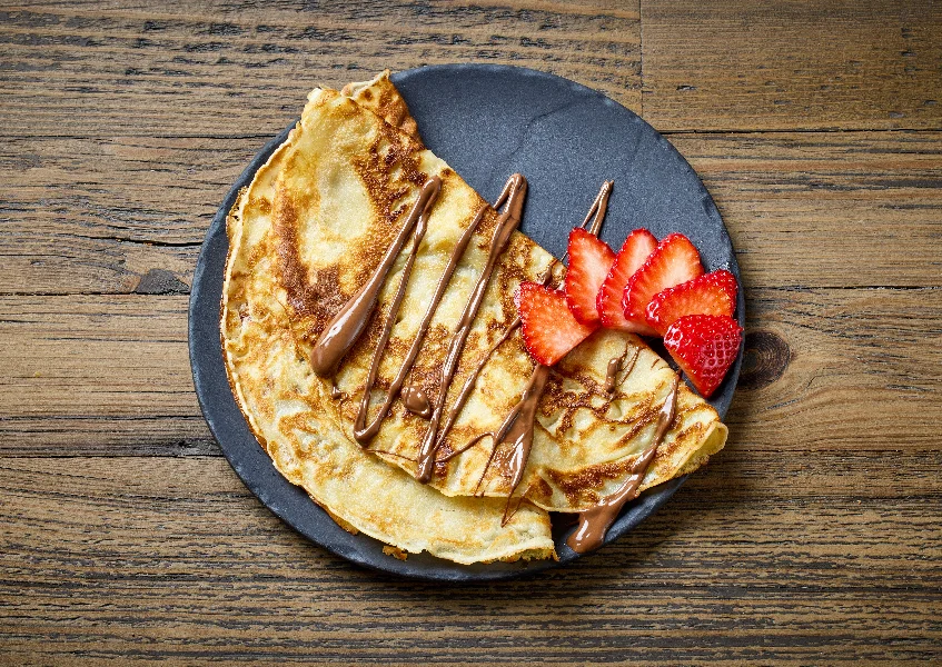 plate of crepes with strawberry and melted chocolate sauce